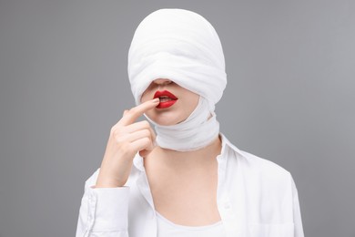 Woman with face wrapped in medical bandage after plastic surgery operation on grey background