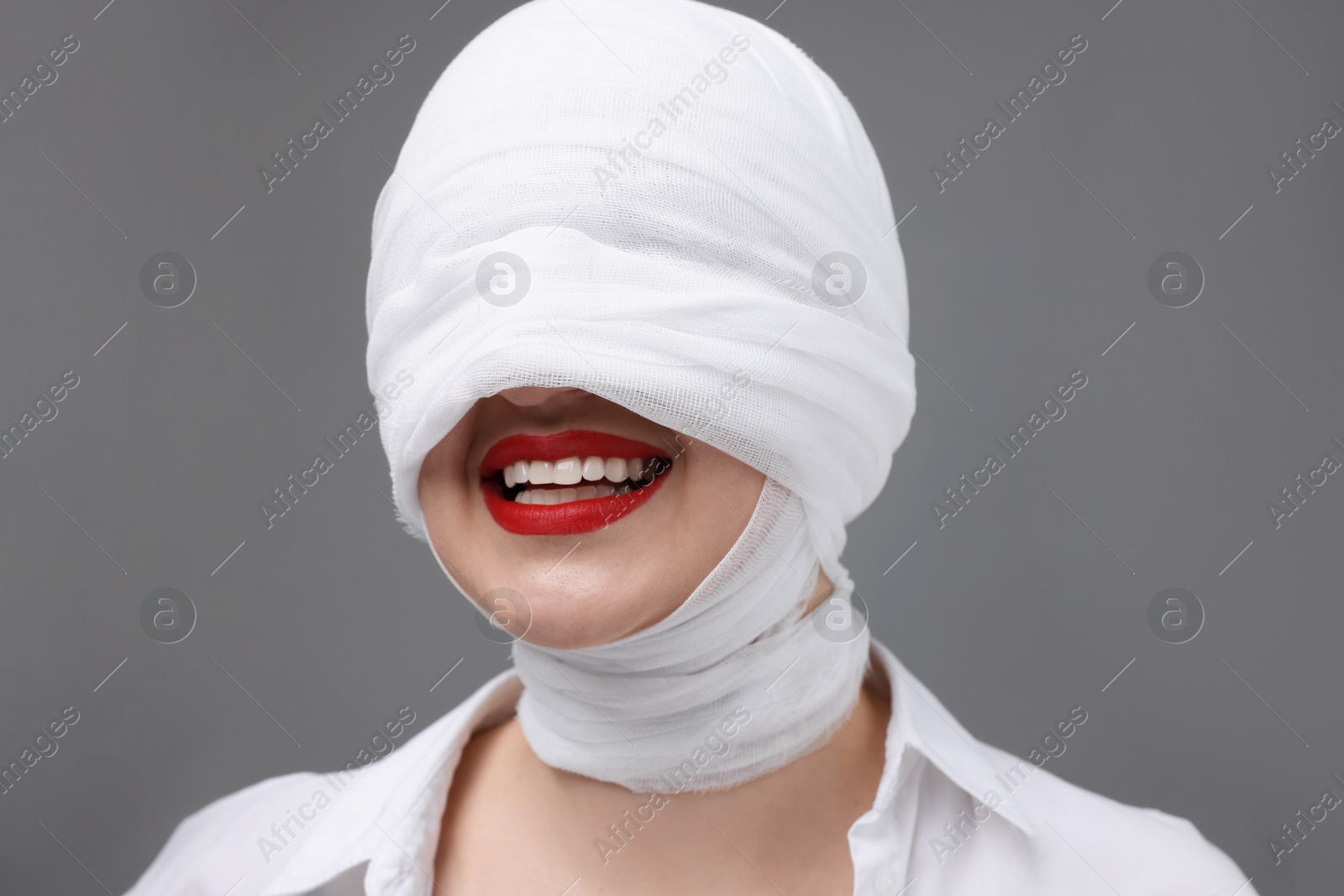 Photo of Woman with face wrapped in medical bandage after plastic surgery operation on grey background