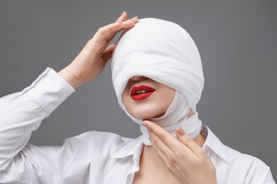 Photo of Woman with face wrapped in medical bandage after plastic surgery operation on grey background