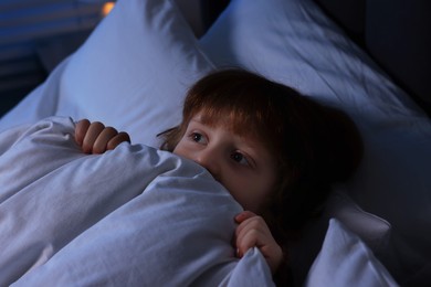 Photo of Scared boy hiding under duvet in bed at night