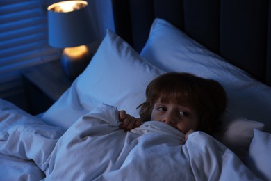 Photo of Scared boy hiding under duvet in bed at night