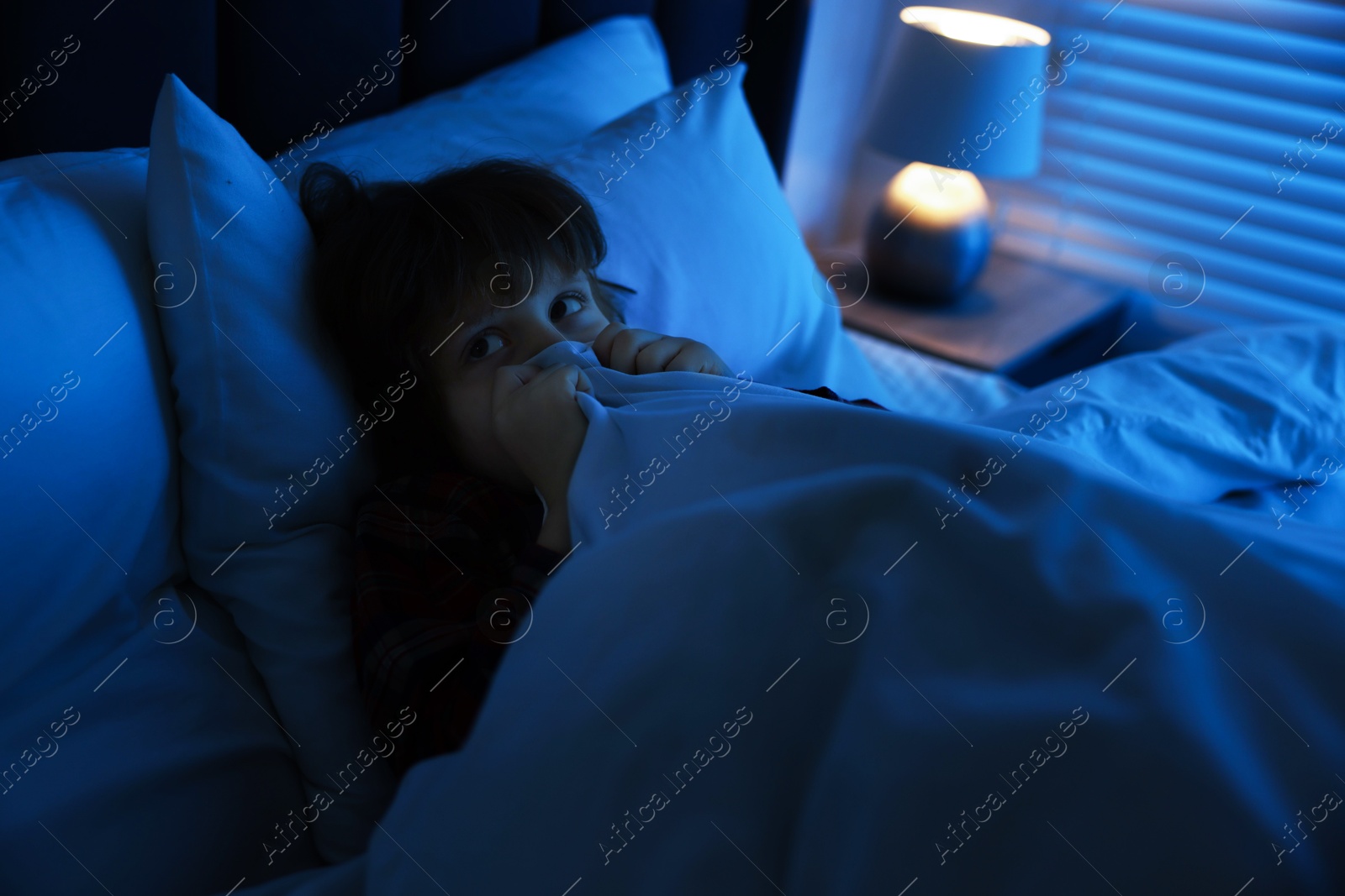 Photo of Scared boy hiding under duvet in bed at night