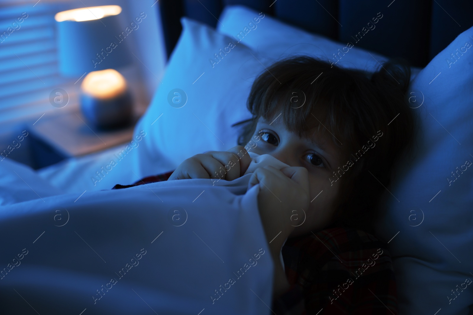 Photo of Scared boy hiding under duvet in bed at night