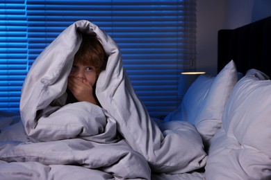 Photo of Scared boy hiding under duvet in bed at night