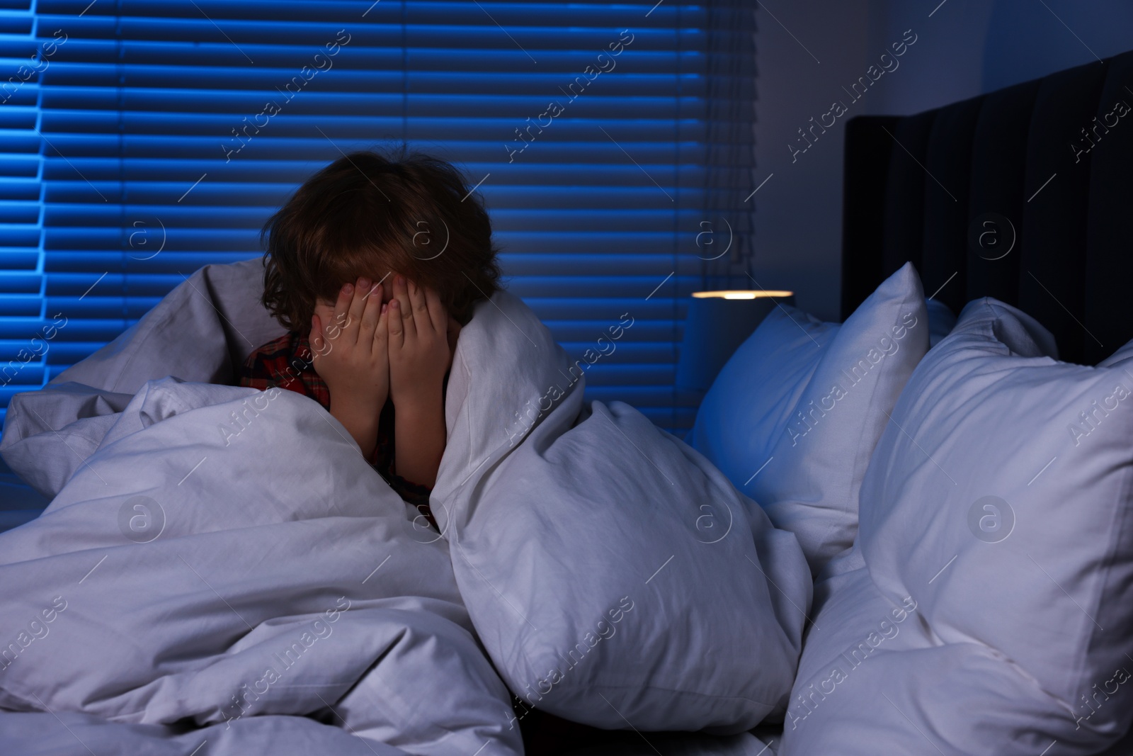 Photo of Scared boy wrapped in duvet on bed at night