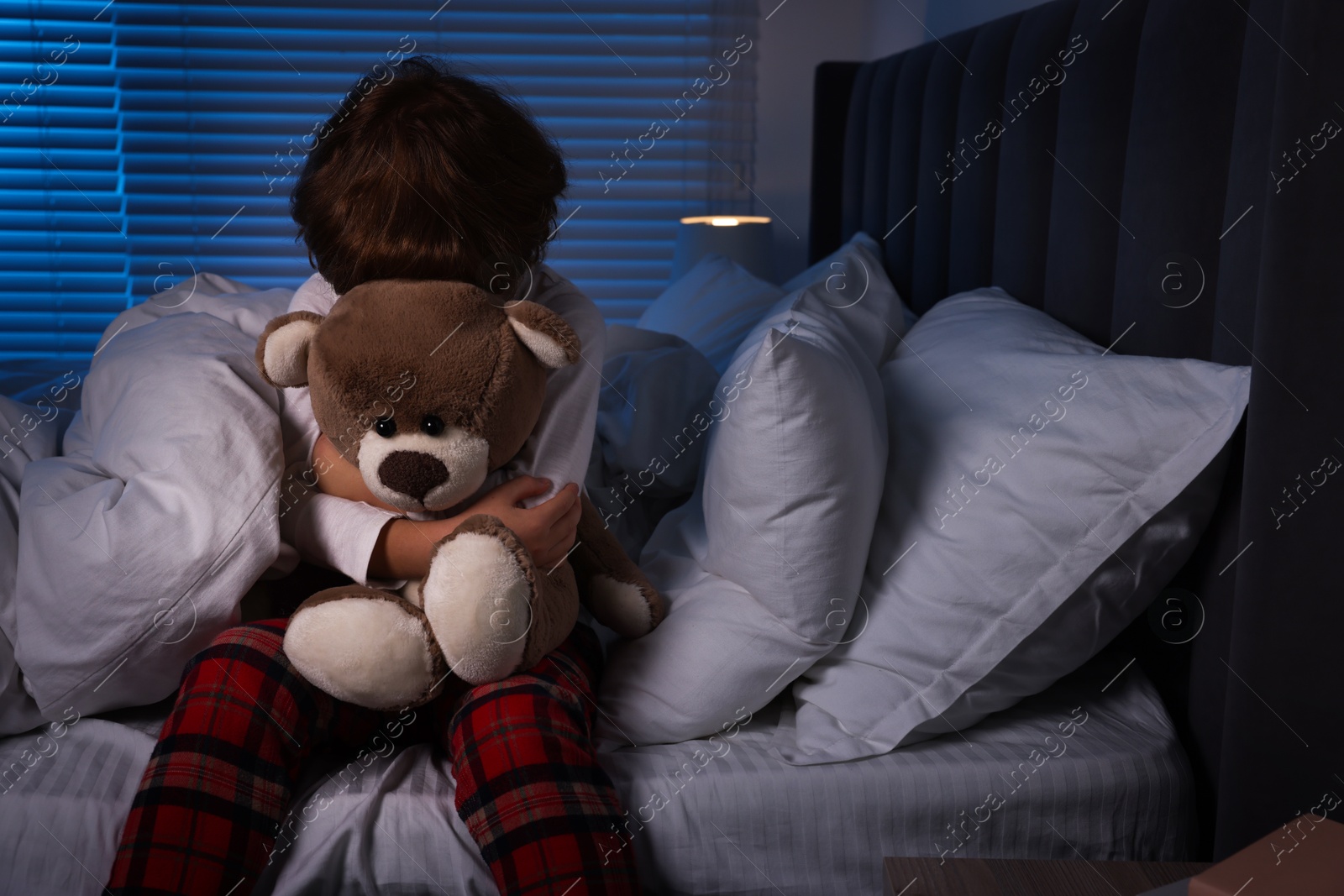 Photo of Scared boy with teddy bear on bed at night