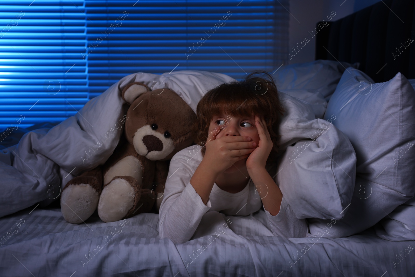 Photo of Scared boy with teddy bear in bed at night