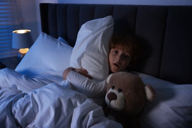 Photo of Scared boy with teddy bear in bed at night