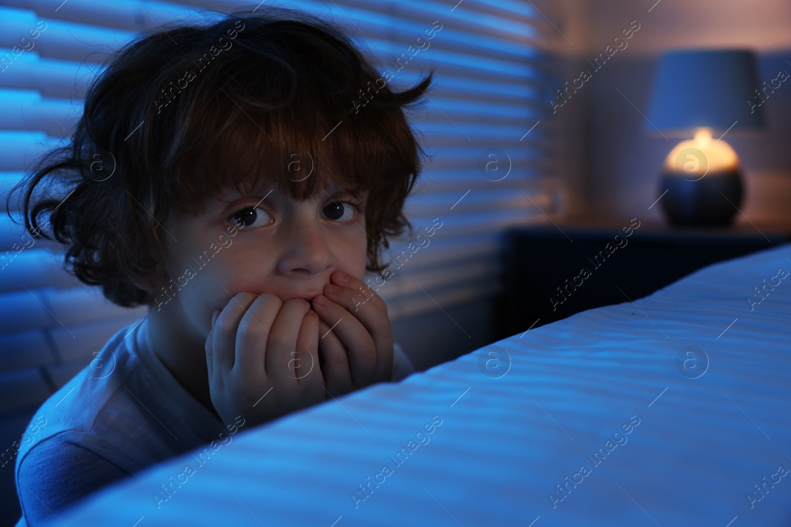 Photo of Scared boy hiding behind bed at night. Space for text