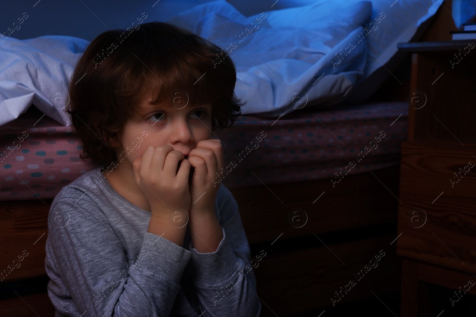 Photo of Afraid boy near his bed at night. Space for text