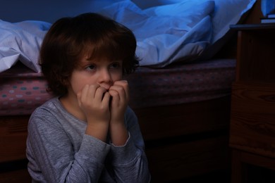 Photo of Afraid boy near his bed at night. Space for text