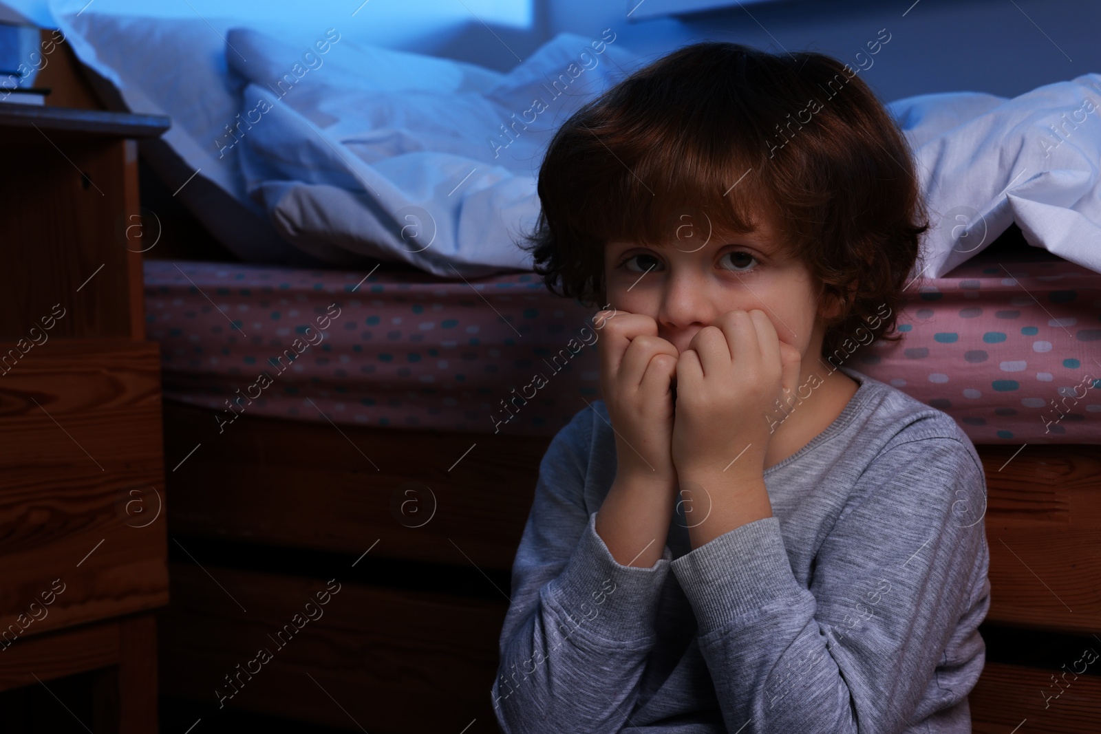 Photo of Afraid boy near his bed at night. Space for text