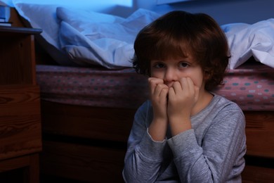 Photo of Afraid boy near his bed at night. Space for text