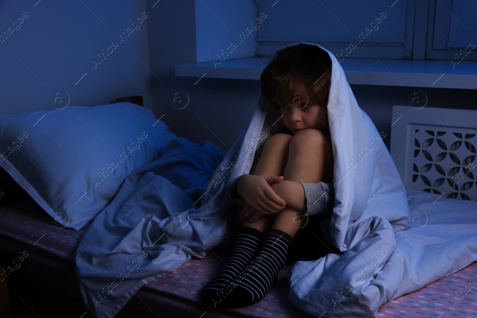 Photo of Afraid boy under blanket on bed at night