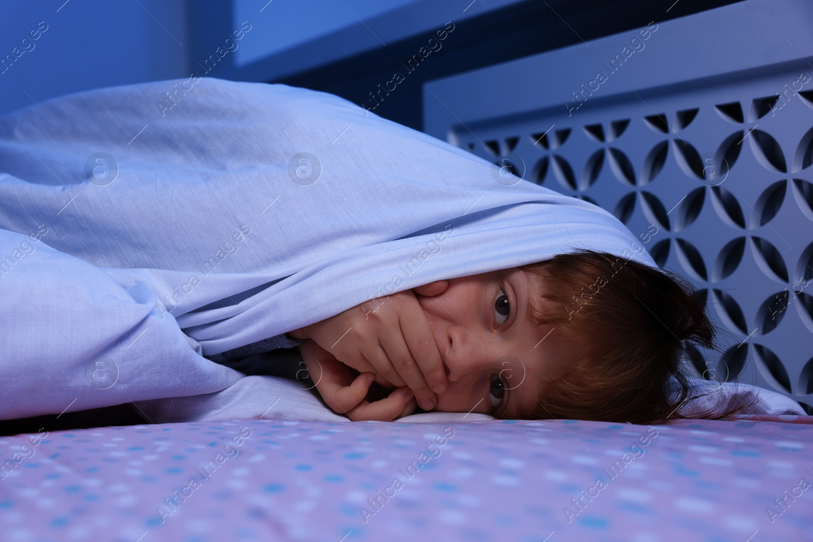 Photo of Afraid boy under blanket on bed at night