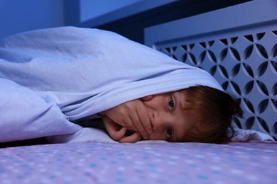 Photo of Afraid boy under blanket on bed at night