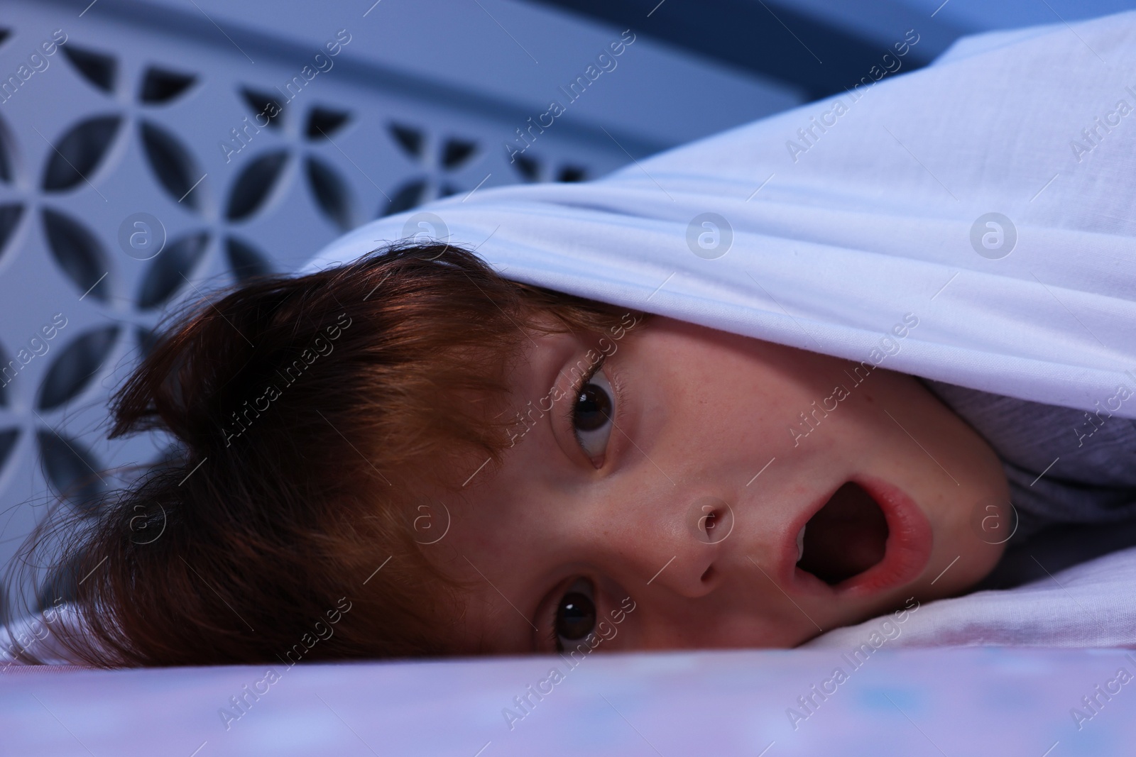 Photo of Afraid boy under blanket on bed at night