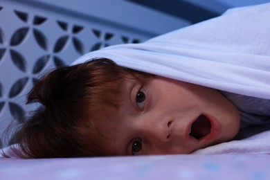 Photo of Afraid boy under blanket on bed at night