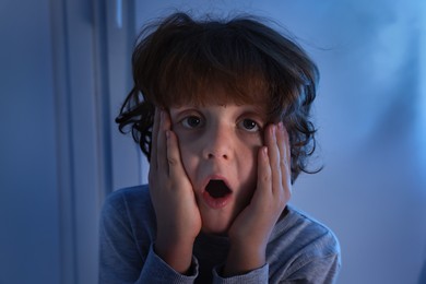 Photo of Scared little boy near window at night