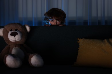 Photo of Fearful boy hiding behind sofa at night