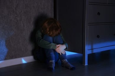 Photo of Scared boy hiding behind chest of drawers at night