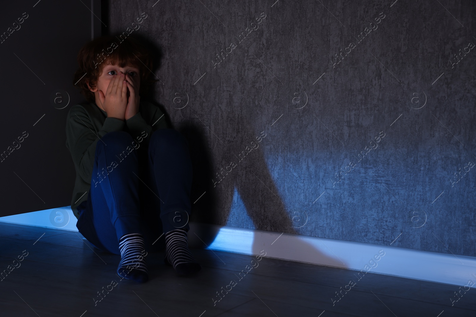 Photo of Scared boy hiding behind chest of drawers at night. Space for text