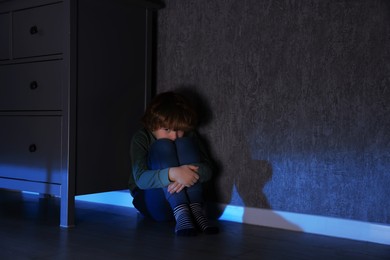 Photo of Scared boy hiding behind chest of drawers at night