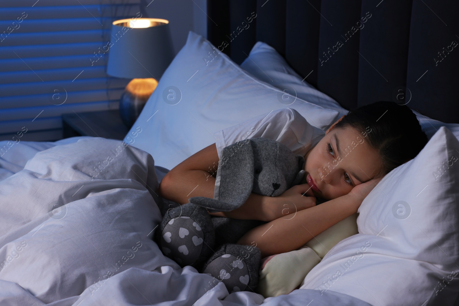 Photo of Scared girl with toy bunny in bed at night