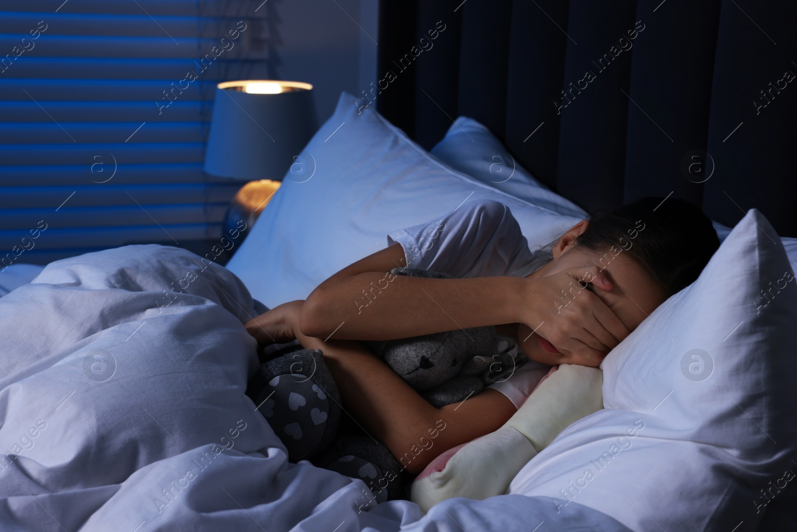 Photo of Scared girl with toy bunny in bed at night