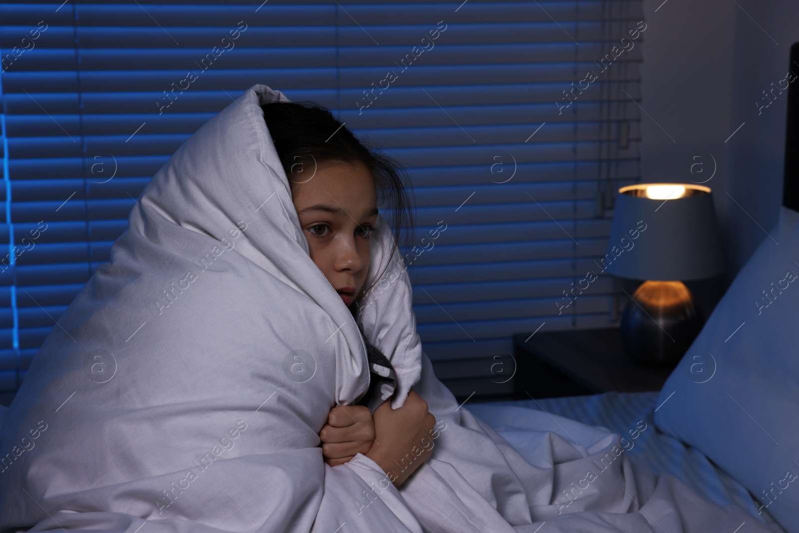 Photo of Afraid girl wrapped in duvet on bed at night. Space for text