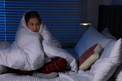 Photo of Afraid girl wrapped in duvet on bed at night