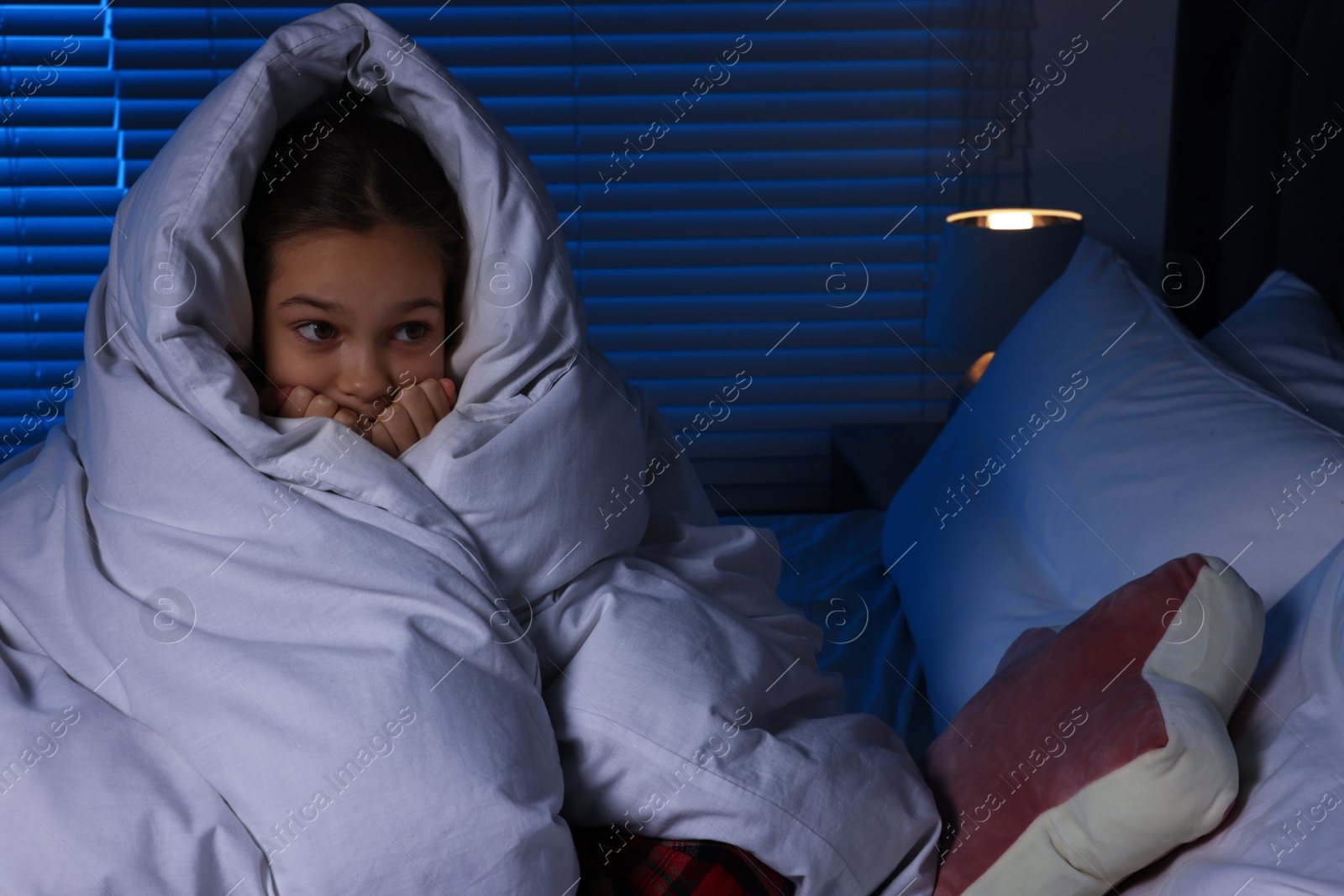 Photo of Afraid girl wrapped in duvet on bed at night