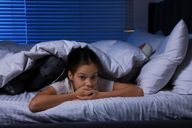 Fearful girl with toy bunny under duvet in bed at night