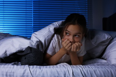 Fearful girl with toy bunny under duvet in bed at night