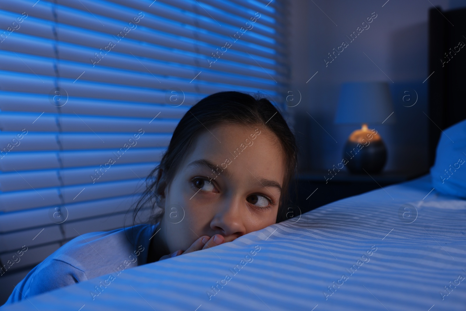 Photo of Scared girl hiding behind bed at night