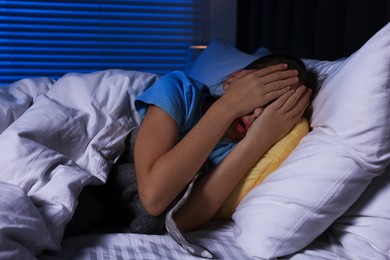 Photo of Scared girl covering face with hands in bed at night