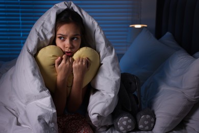 Photo of Afraid girl with pillow under duvet on bed at night