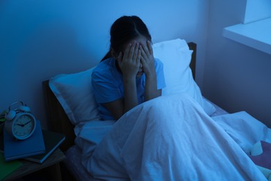 Photo of Afraid girl covering face with hands in bed at night