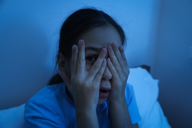 Photo of Afraid girl covering face with hands in bed at night