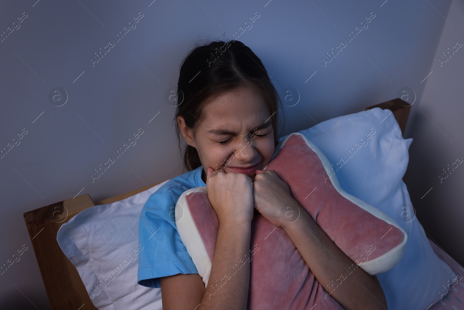 Photo of Afraid girl with pillow in bed at night