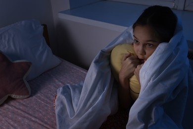 Photo of Afraid girl with pillow under duvet on bed at night. Space for text