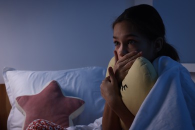 Afraid girl with pillow under duvet on bed at night. Space for text