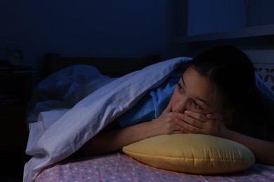 Photo of Afraid girl with pillow under duvet on bed at night