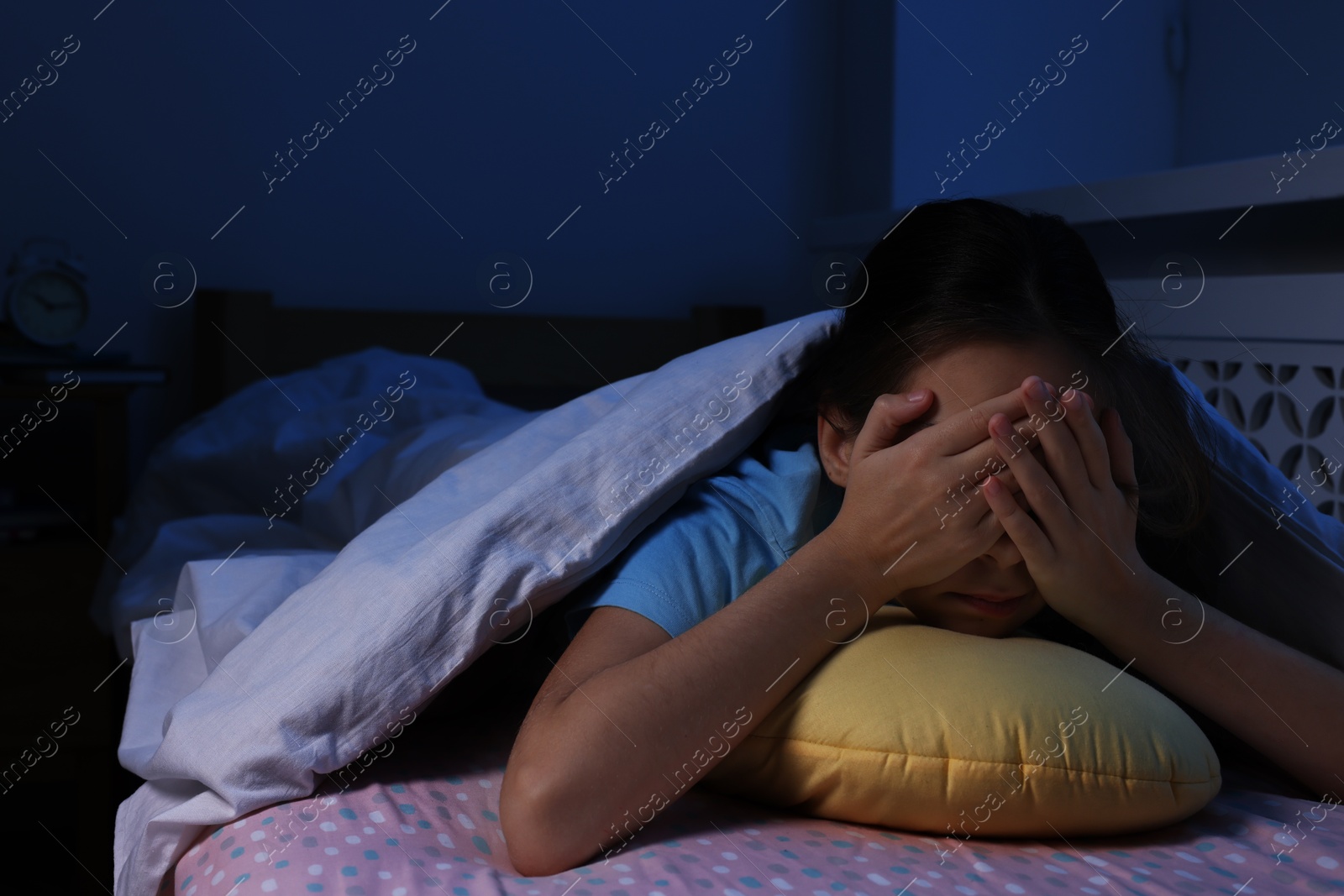 Photo of Afraid girl with pillow under duvet on bed at night