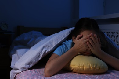 Photo of Afraid girl with pillow under duvet on bed at night