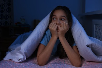 Photo of Afraid girl hiding under duvet on bed at night