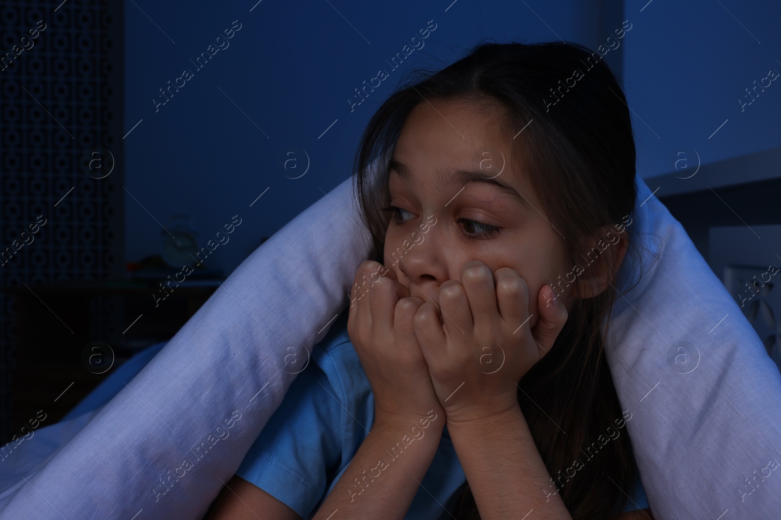 Photo of Afraid girl hiding under duvet on bed at night