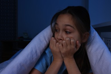 Photo of Afraid girl hiding under duvet on bed at night