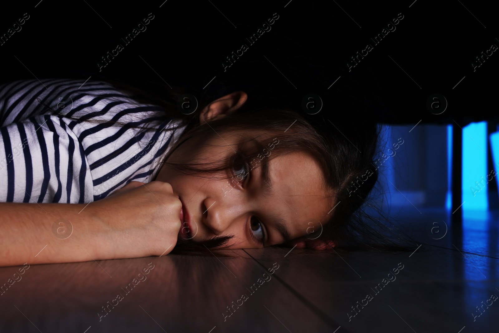 Photo of Fearful girl hiding under bed at night