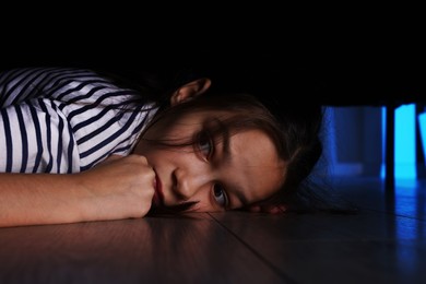 Fearful girl hiding under bed at night